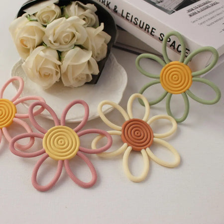 Ensemble d'anneaux de dentition fleurs colorées posés près de roses blanches - Bébé Lova