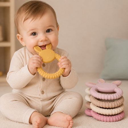 Bébé mordillant un anneau de dentition lapin jaune en silicone avec pile d’anneaux pastel à côté - Bébé Lova