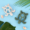 Deux anneaux de dentition tortue en silicone posés sur fond bleu tropical - Bébé Lova