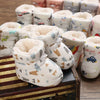 Plusieurs paires de bottines bébé fourrées à imprimés variés posées sur une valise vintage - Bébé Lova