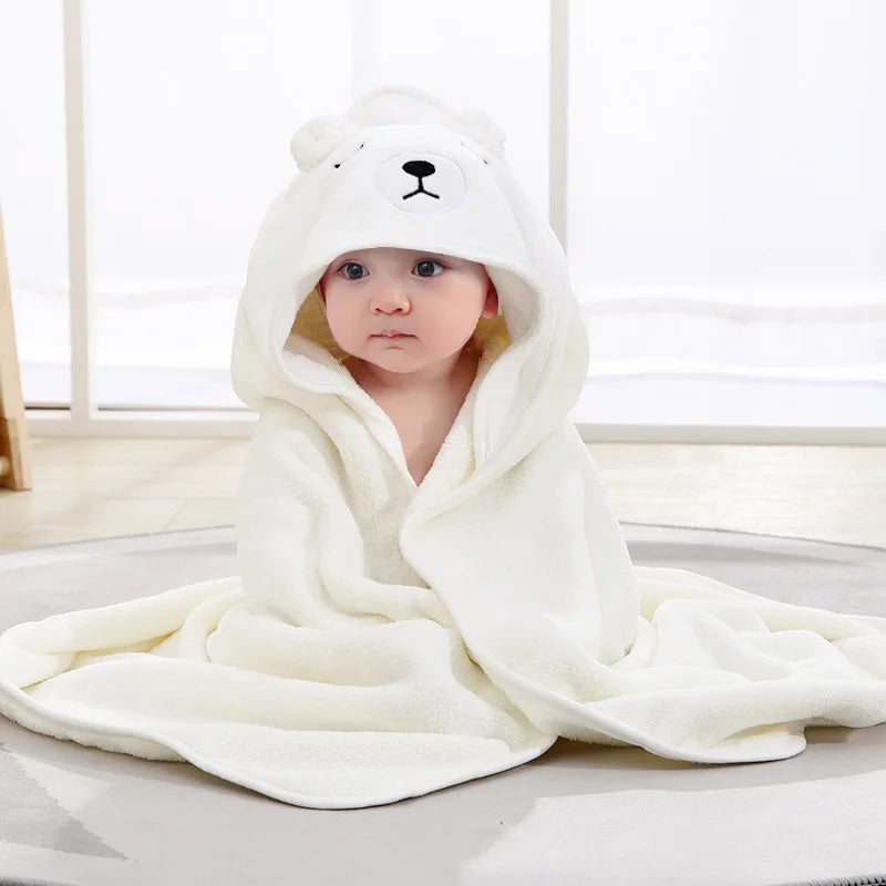 Bébé enveloppé dans une cape de bain BathCape blanche à capuche ourson assis sur un tapis - Bébé Lova