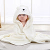 Bébé enveloppé dans une cape de bain BathCape blanche à capuche ourson assis sur un tapis - Bébé Lova