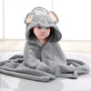 Bébé enveloppé dans une cape de bain BathCape grise à capuche éléphant assis sur un tapis - Bébé Lova