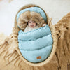 Bébé souriant installé dans une chancelière évolutive bleu ciel avec capuche en fausse fourrure dans un panier en osier confortable - Bébé Lova