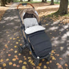 Chancelière noire installée sur une poussette dans un parc en automne - Bébé Lova