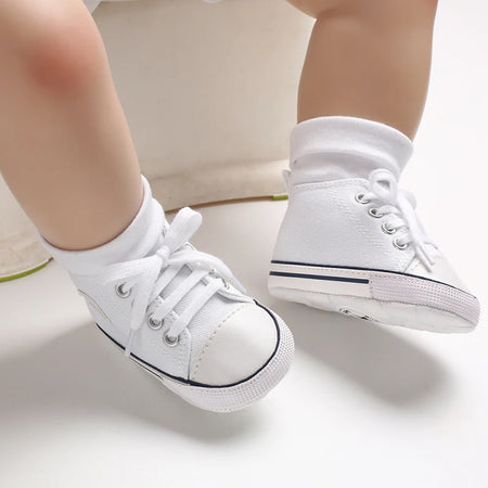Gros plan sur les pieds d'un bébé portant des chaussures en toile blanches et des chaussettes blanches - Bébé Lova
