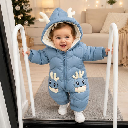 Bébé souriant debout portant la combinaison d'hiver matelassée bleue à capuche bois de cerf dans un salon de Noël - Bébé Lova