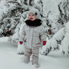 Bébé souriant dans la neige portant l'ensemble de ski gris clair avec bonnet à pompon - Bébé Lova