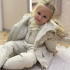 Petite fille assise en intérieur portant l'ensemble de ski beige à capuche fourrée - Bébé Lova