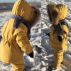 Enfant de dos dans la neige portant l'ensemble de ski jaune moutarde à capuche fourrée - Bébé Lova