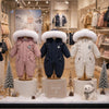 Combinaisons de ski bébé rose, bleu marine et blanche présentées en vitrine dans une ambiance hivernale - Bébé Lova