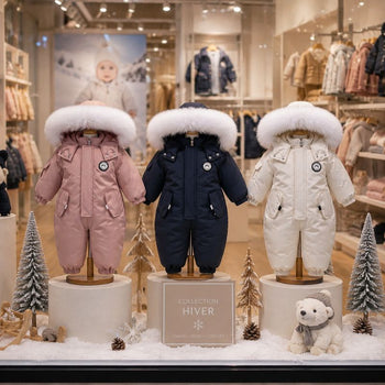 Combinaisons de ski bébé rose, bleu marine et blanche présentées en vitrine dans une ambiance hivernale - Bébé Lova