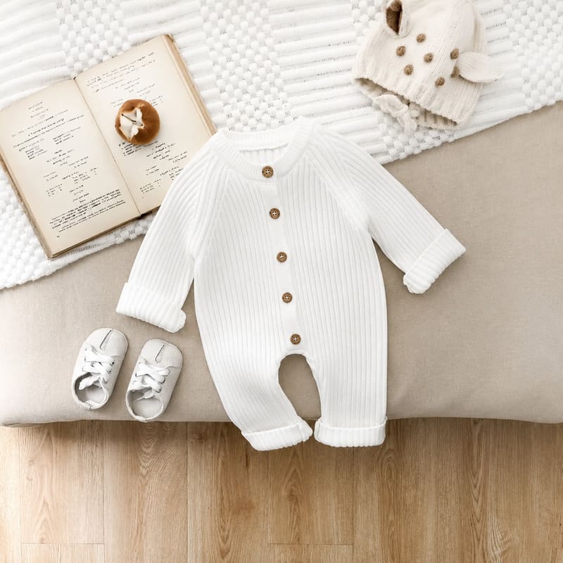 Combinaison tricot bébé blanche mise en scène avec livre et chaussons - Bébé Lova