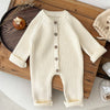 Combinaison tricot bébé écru présentée pliée sur un plateau en bois avec bonnet - Bébé Lova