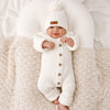 Combinaison tricot bébé blanche portée par un bébé souriant avec bonnet à pompon - Bébé Lova