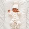 Combinaison tricot bébé blanche portée par un nouveau-né endormi avec bonnet à pompon et chaussons - Bébé Lova