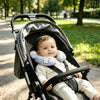 Bébé installé en poussette dans un parc avec le coussin de nuque gris nuages - Bébé Lova