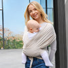 Écharpe de portage bébé extensible en coton coloris beige portée par une maman souriante en extérieur - Bébé Lova