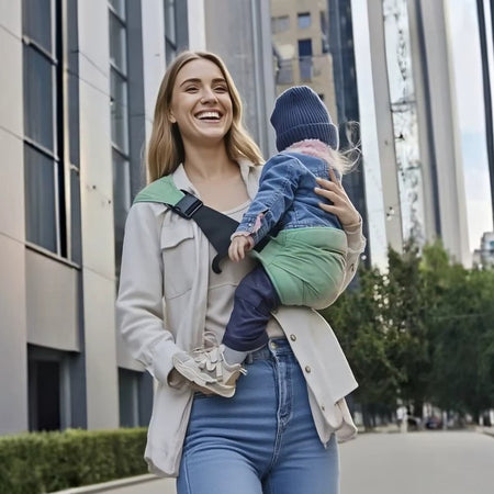 Maman souriante portant son enfant dans l'écharpe sling verte en ville - Bébé Lova