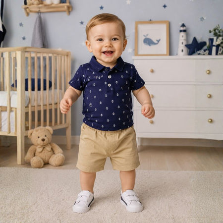 Bébé garçon souriant debout dans une chambre portant l'ensemble polo marine à ancres et short beige - Bébé Lova