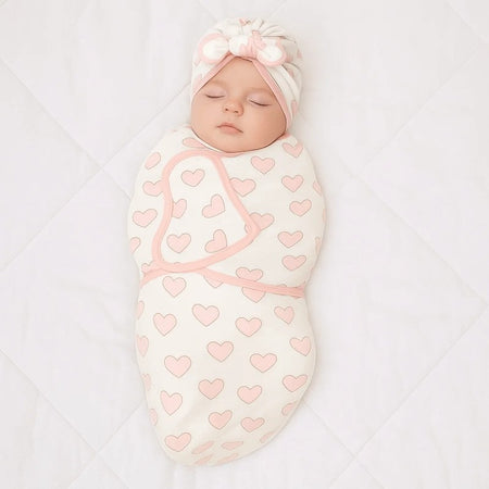 Bébé emmailloté vu de dessus dans la gigoteuse motif cœur rose avec son bonnet turban à nœud - Bébé Lova