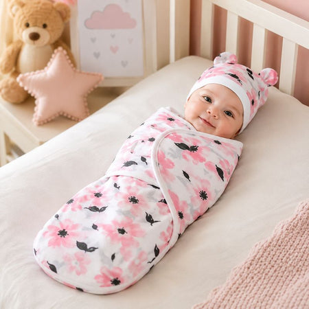 Bébé emmailloté dans un lange fleuri rose avec bonnet assorti dans une chambre cocooning - Bébé Lova