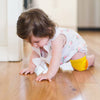 Bébé portant des genouillères jaunes antidérapantes sur parquet en bois - Bébé Lova