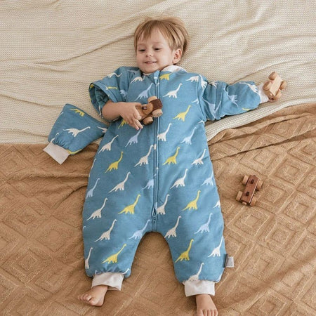 Enfant allongé avec gigoteuse bleue motif dinosaures et manches amovibles sur lit beige - Bébé Lova