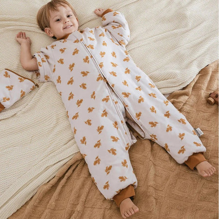 Enfant souriant allongé avec gigoteuse blanche à motifs feuilles dorées sur couverture douce - Bébé Lova