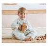 Bébé assis sur un lit avec gigoteuse verte matelassée motif feuilles et jouets en bois - Bébé Lova