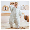 Enfant debout avec gigoteuse verte motif feuillage tenant un appareil photo en bois - Bébé Lova