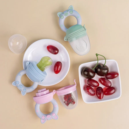 Grignoteurs de fruits en silicone vert, bleu et rose présentés avec des raisins et des cerises frais - Bébé Lova
