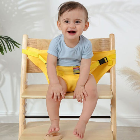 Harnais de sécurité pour chaise bébé coloris jaune porté par un bébé souriant sur une chaise en bois - Bébé Lova