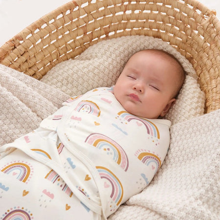Bébé endormi emmailloté dans un lange swaddle coton avec motifs arc-en-ciel dans un panier en osier - Bébé Lova