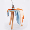 Langes en mousseline de bambou orange, bleu et écru drapés sur un tabouret en bois - Bébé Lova