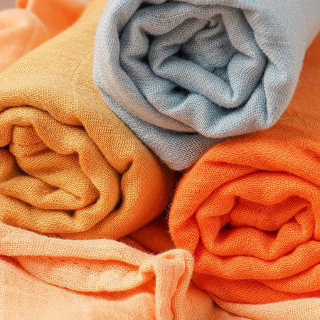 Gros plan sur la texture des langes en mousseline de bambou roulés jaune, bleu et orange - Bébé Lova