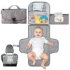 Bébé souriant allongé sur le matelas à langer portable AquaMom gris déplié avec poches filet garnies - Bébé Lova