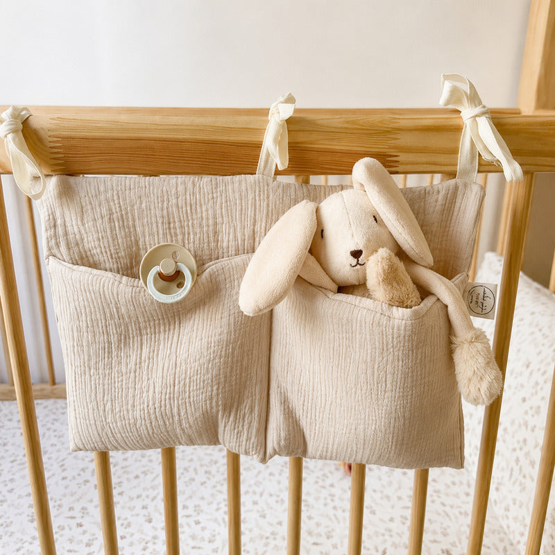 Organiseur de lit beige suspendu à un berceau en bois avec doudou lapin et tétine - Bébé Lova