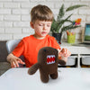 Enfant en t-shirt orange découvrant une peluche monstre kawaii Funny Domo sur une table - Bébé Lova