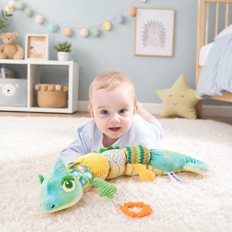 Bébé allongé dans une chambre d’enfant avec la peluche musicale caméléon sensorielle - Bébé Lova