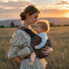 Maman portant bébé face à elle dans le porte-bébé léopard bandoulière LeoParry lors d'une balade au coucher du soleil - Bébé Lova