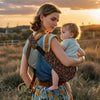 Maman en promenade au coucher du soleil portant bébé sur la hanche avec le porte-bébé léopard LeoParry - Bébé Lova