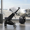 Poussette de voyage AirFold dépliée dans un aéroport face à un avion, avec sa version pliée transformée en sac à dos - Bébé Lova