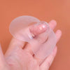 Protège-mamelon en silicone tenu au bout du doigt montrant sa finesse, sur fond orange - Bébé Lova
