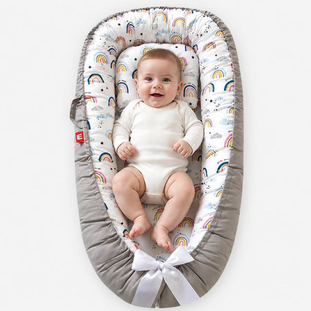 Réducteur de lit bébé avec motifs arc-en-ciel et bébé allongé confortablement - Bébé Lova