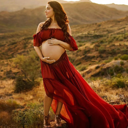 Future maman en robe rouge fluide posant dans un paysage désertique au coucher du soleil - Bébé Lova