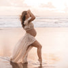 Femme enceinte marchant sur la plage au coucher du soleil avec une robe beige aérienne - Bébé Lova