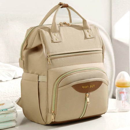 Sac à dos à langer beige vu de trois quarts montrant ses multiples poches zippées et finitions dorées - Bébé Lova