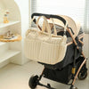 Sac à langer beige suspendu à une poussette grâce aux attaches intégrées - Bébé Lova