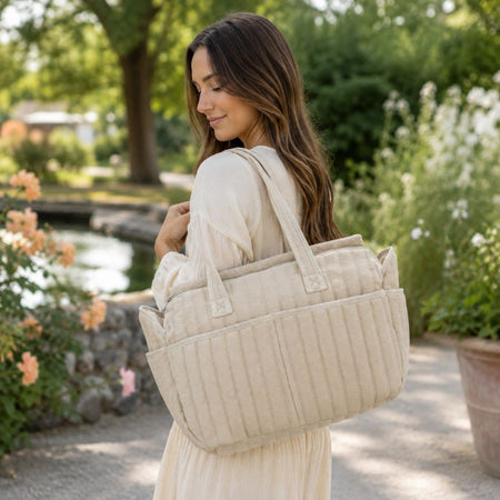 Maman portant le sac à langer beige dans un jardin lumineux en extérieur - Bébé Lova